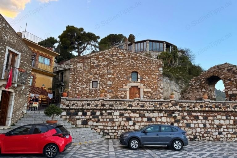 Autos vor einer Mauer, einem Haus und einem Boge aus Stein