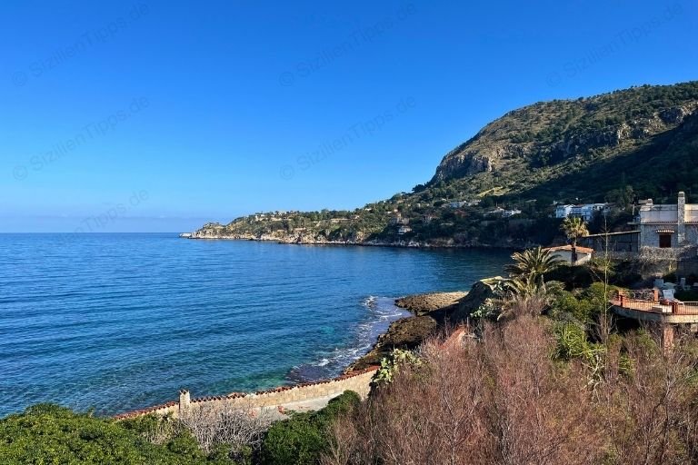 Eine Bucht mit Büschen und Villen unter blauem Himmel.