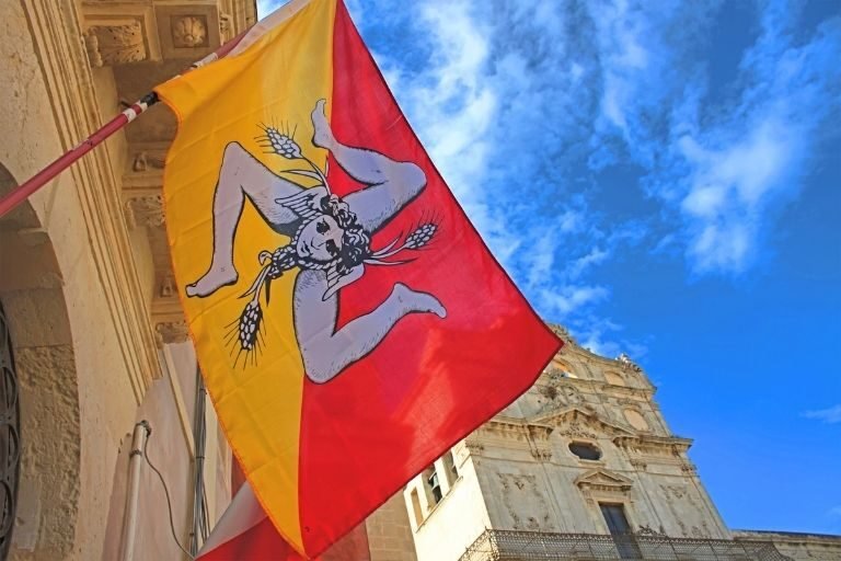 Eine rot-gelbe Flagge mit einem Gesicht, 3 Beinen und Getreideähren