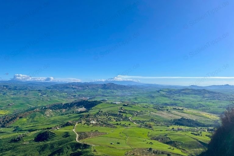 Siziliens grüne Hügel und der Vulkan Ätna im Hintergrund unter blauem Himmel