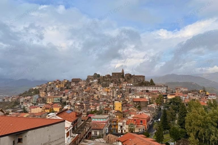 Dorf mit Kirche vor Bergen unter bewölktem Himmel